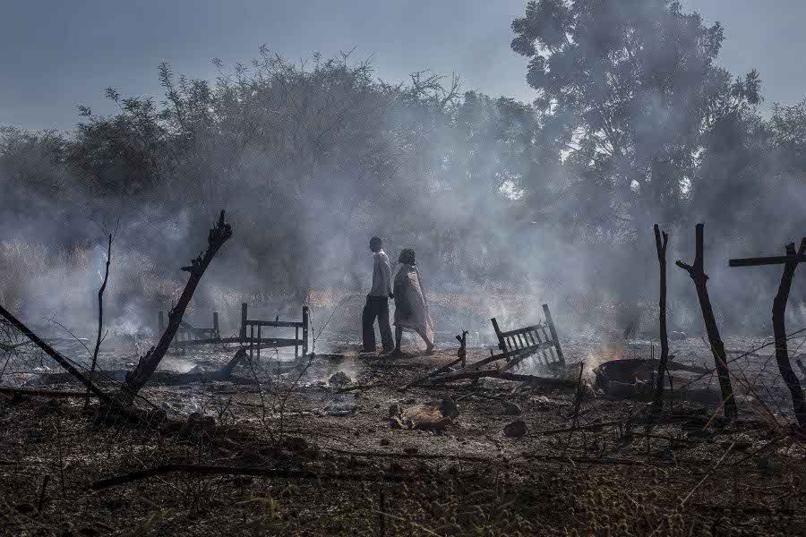 Après le bombardement du village de Kauda, un couple marche dans les cendres de la maison qui a été détruite. Cette offensive a détruit quatres maisons, ainsi que toutes les récoltes annuelles qui venaient d'être collectées. Les familles n'auront plus de nourriture jusqu'à la prochaine récolte en Septembre de l'année suivante. November 2012 After the bombing in Kauda, a couple walks on the ashes of a house that got torn down. The bombardments destroyed four houses as well as all the crops leaving families with no food until the next recolt in September 2013. Kauda, South Kordofan, Sudan - November 2012